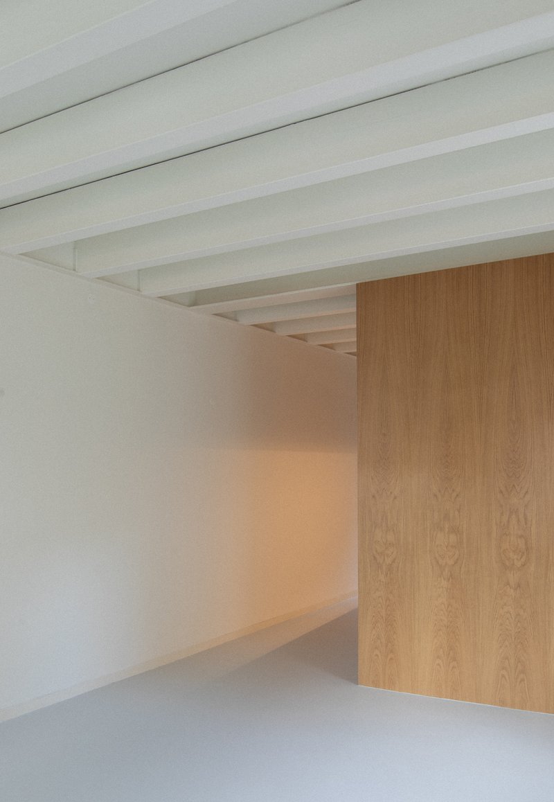 Corner detail where white ceiling beams meet a freestanding oak veneer cabinet partition