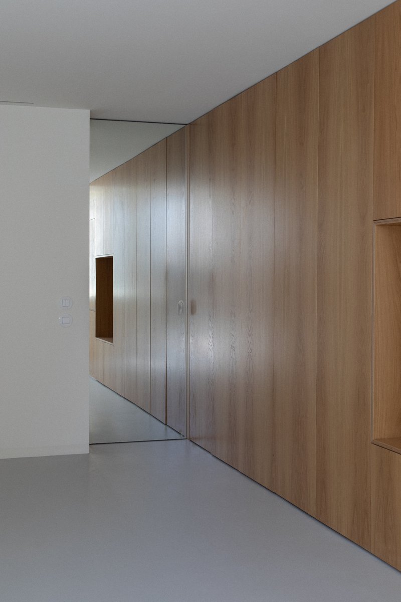 Angled oak veneer wall with small square opening above grey resin floor