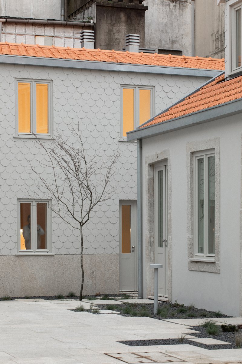 Facade clad in white scalloped tiles with double-hung windows and terra-cotta roof beside a bare winter tree