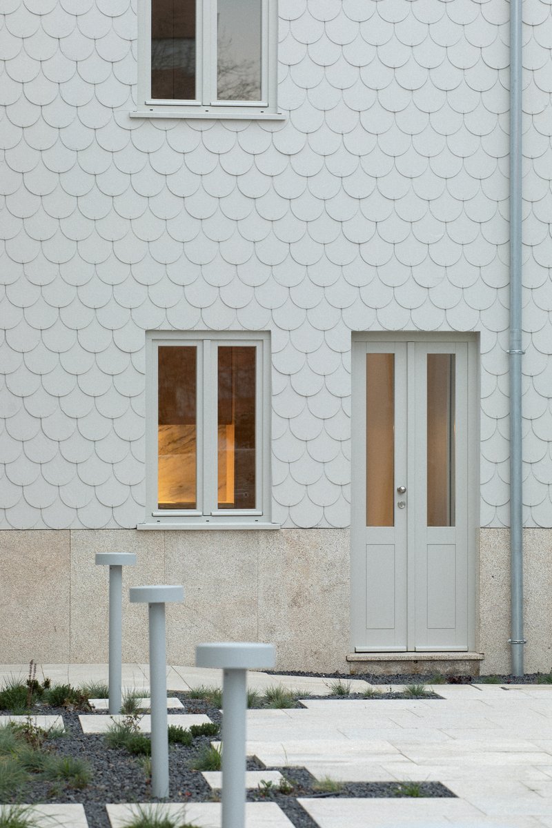 Close-up of scalloped tile cladding above a granular base with steel posts punctuating the paved ground plane