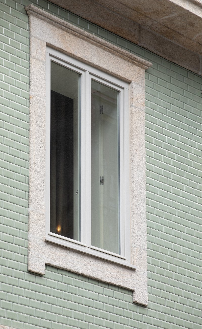 Detail of a white casement window framed in terrazzo surround against pale green glazed tile cladding