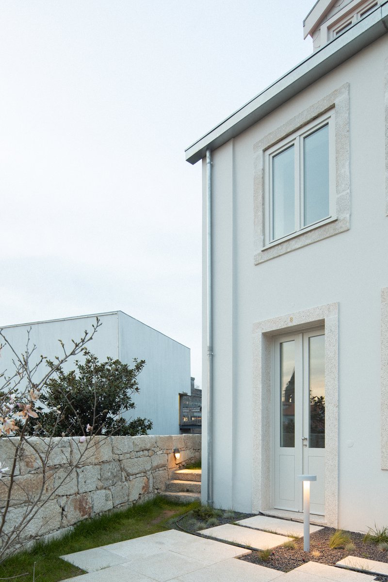 White rendered facade with stone window surrounds beside a low granite wall at dusk