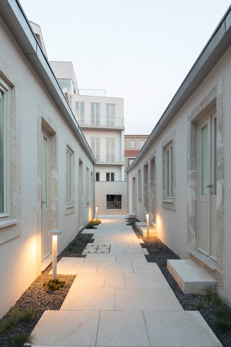 Linear courtyard with pale stone paving and uplighting between two white rendered blocks at dusk