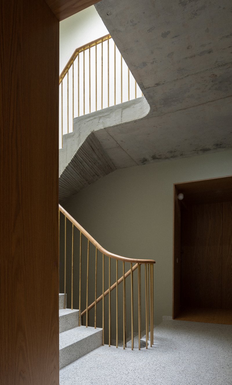 Timber-railed staircase with terrazzo treads framed by exposed concrete ceiling and wood-paneled walls