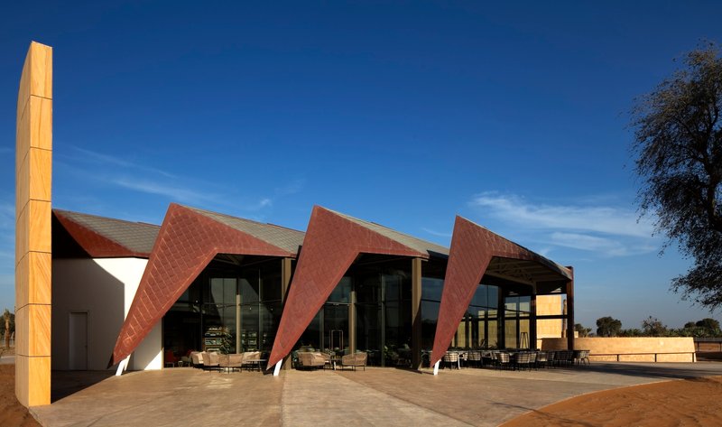 Facade with angled copper-clad panels and glass walls opening to a stone terrace at dusk