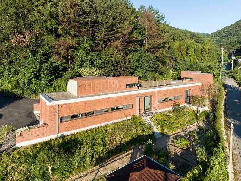 Aerial view of the stacked brick volumes and rooftop terrace surrounded by dense summer foliage