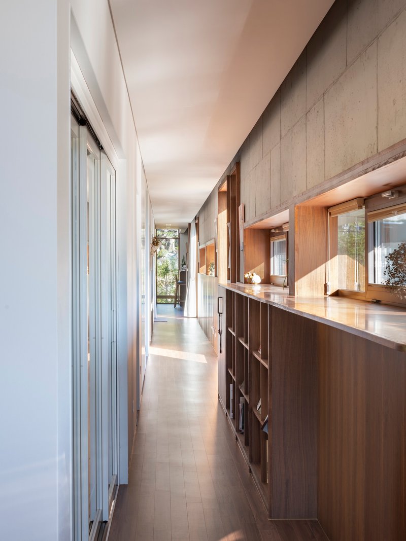 Corridor with board-formed concrete wall and timber cabinetry lit by clerestory windows