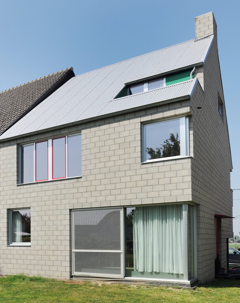 Side facade displaying pale masonry walls, corrugated roof slope, and stacked window openings with green accents