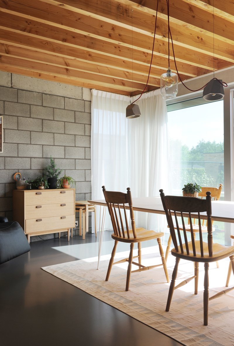 Dining area with timber ceiling joists and large corner window framing green landscape beyond white curtains