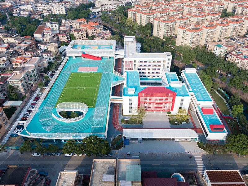 Aerial view of the school campus with turquoise running track, soccer pitch and white buildings set in dense residential neighborhood