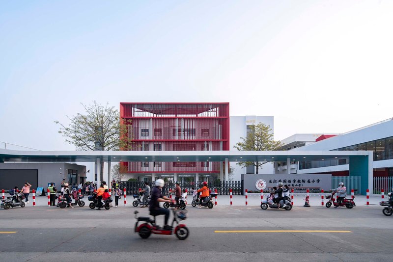 Street view of the red louvered facade and elevated pedestrian bridge with scooters passing by at dusk