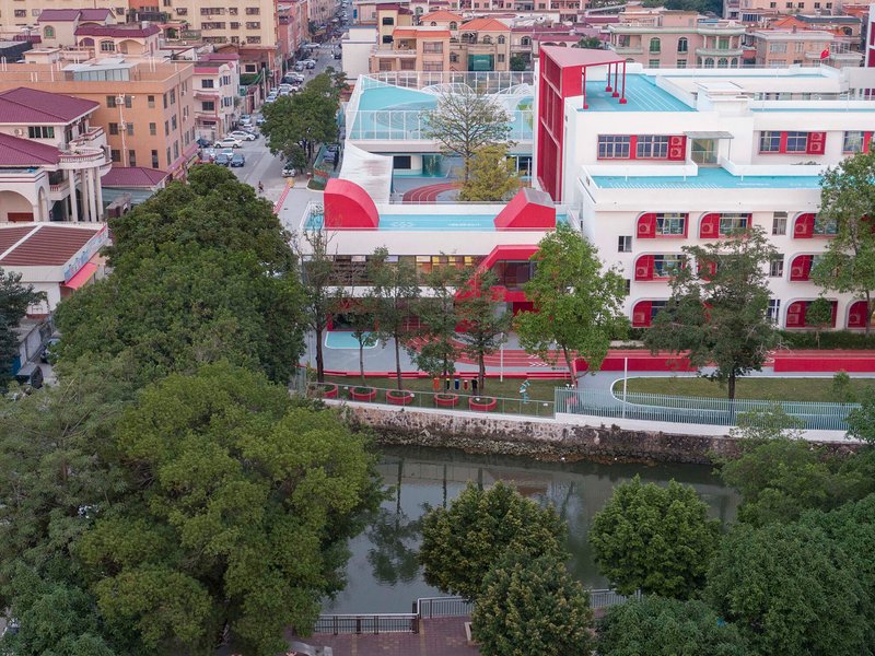 Campus buildings with red accents and white volumes set along a tree-lined canal at twilight