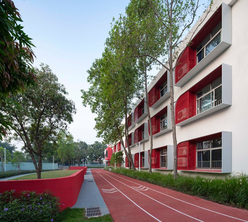 White facade with red panel openings facing a red running track lined with birch trees