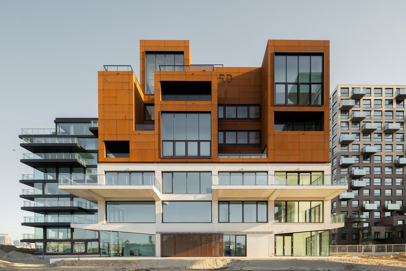 Articulated facade combining weathered steel panels and stacked white balconies on raw ground