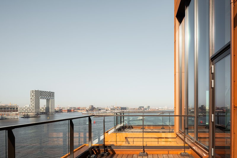 Rooftop terrace with timber decking and glass balustrade facing a river at dusk