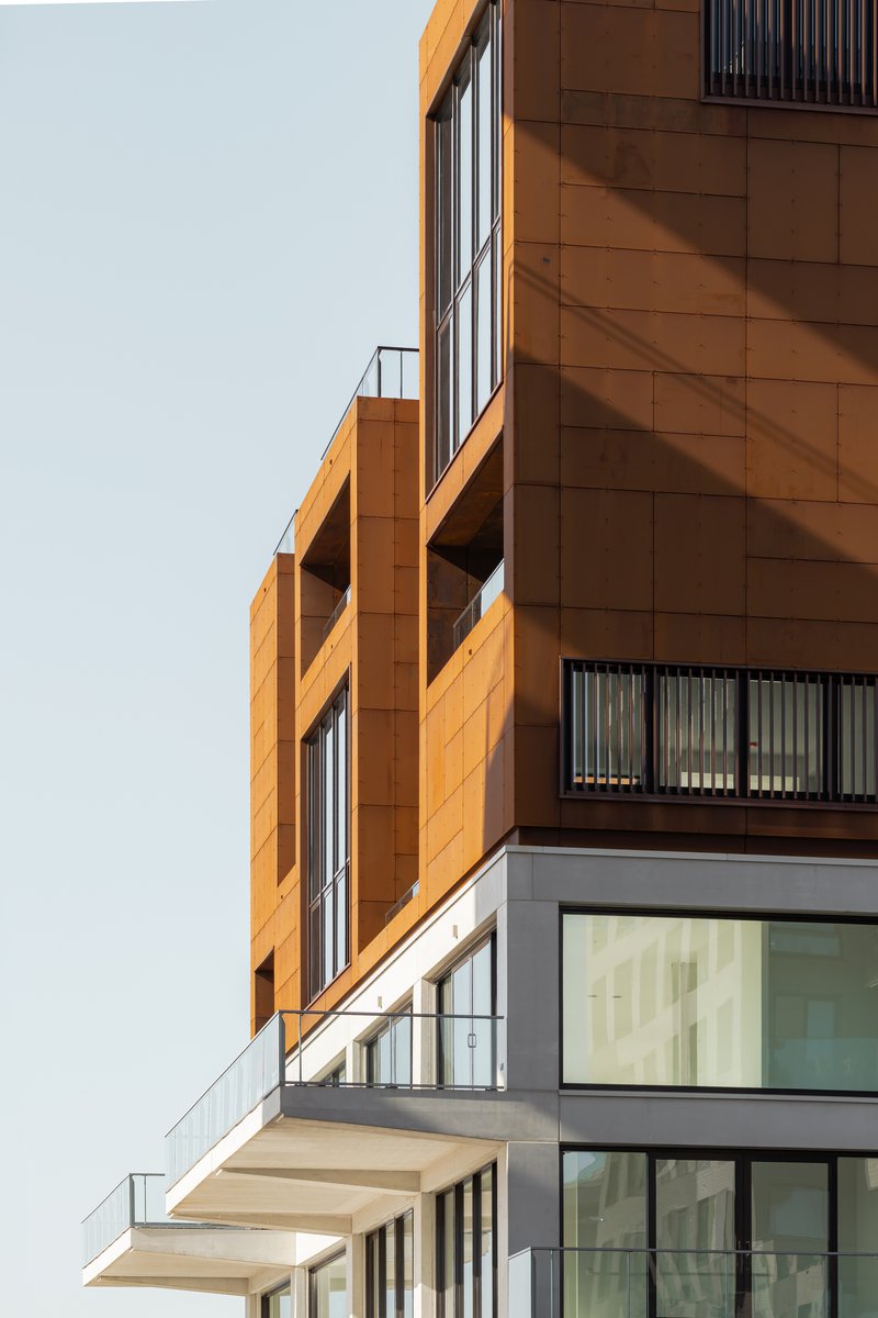 Stacked balconies with orange and grey cladding and cantilevered terraces in afternoon light