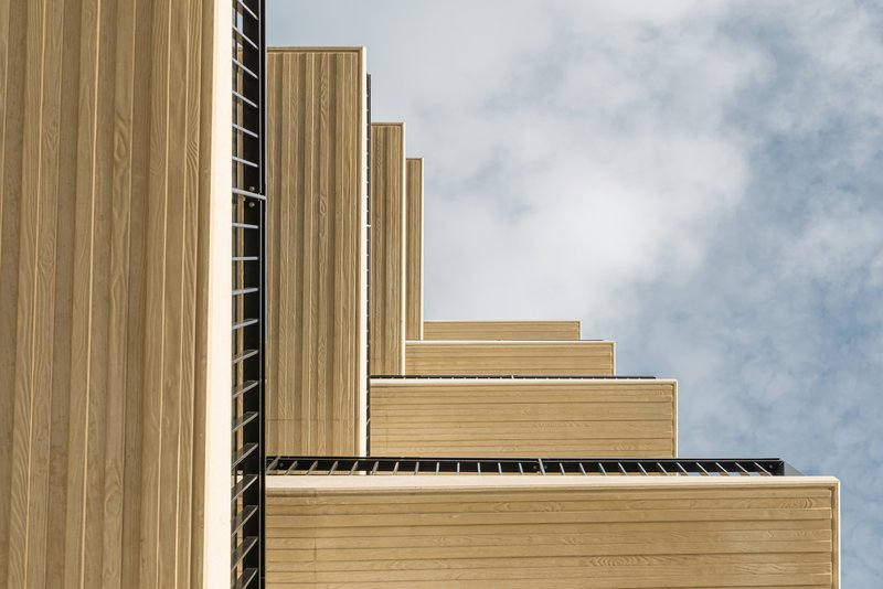 Stepped timber-clad facade with vertical battens rising against a cloudy sky