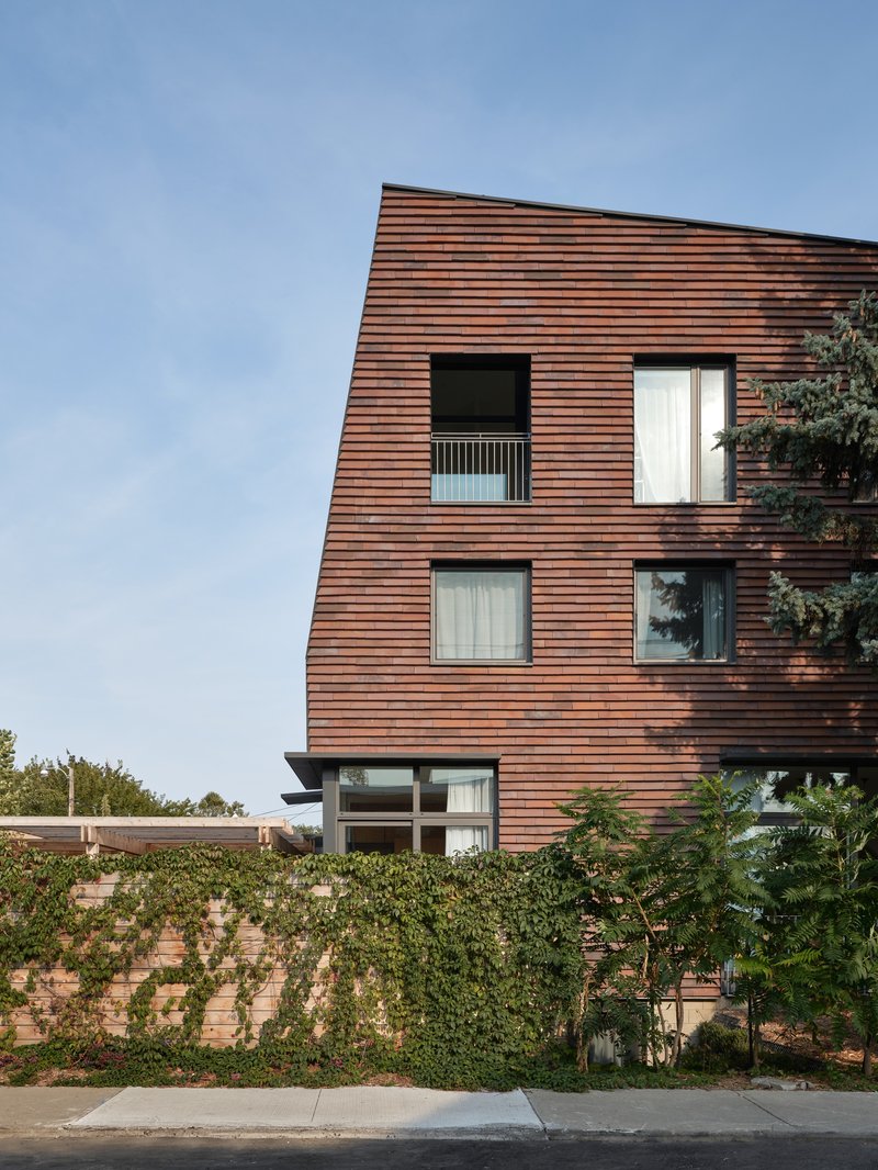 Three-storey copper facade with inset balcony above a vine-covered brick wall at street level