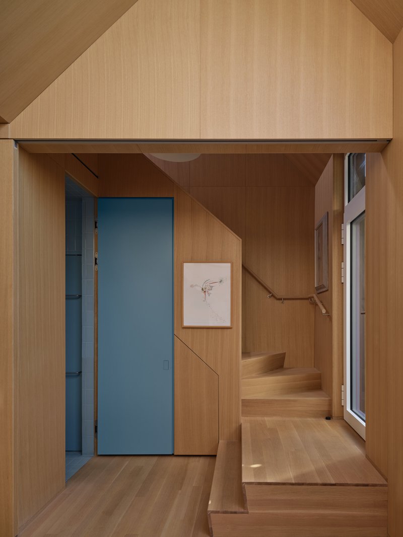 Timber-lined stairwell with flush blue door, built-in seating, and handrail following the ascent