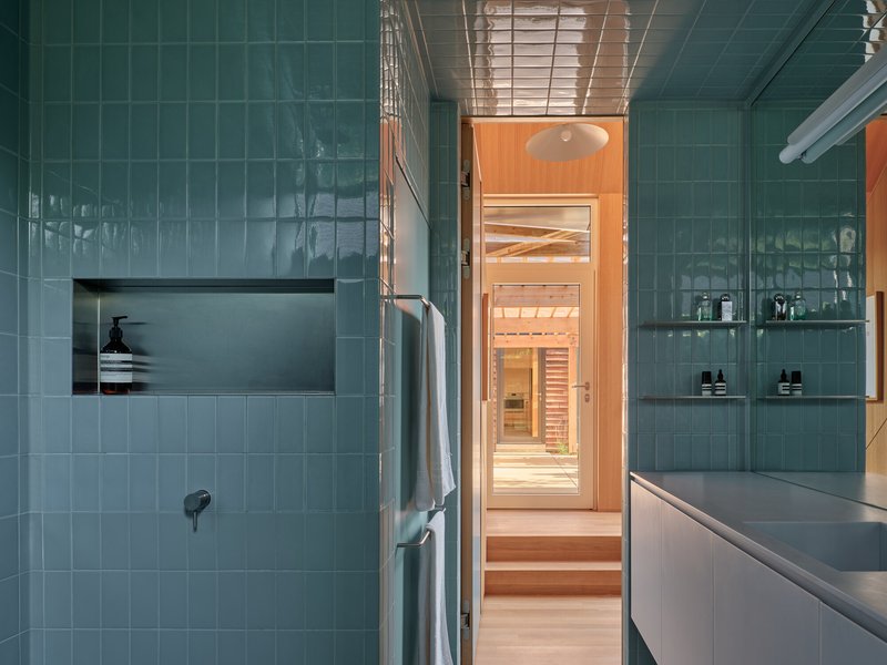 Green tile bathroom with recessed niche, glass shelving, and view through to the sauna beyond