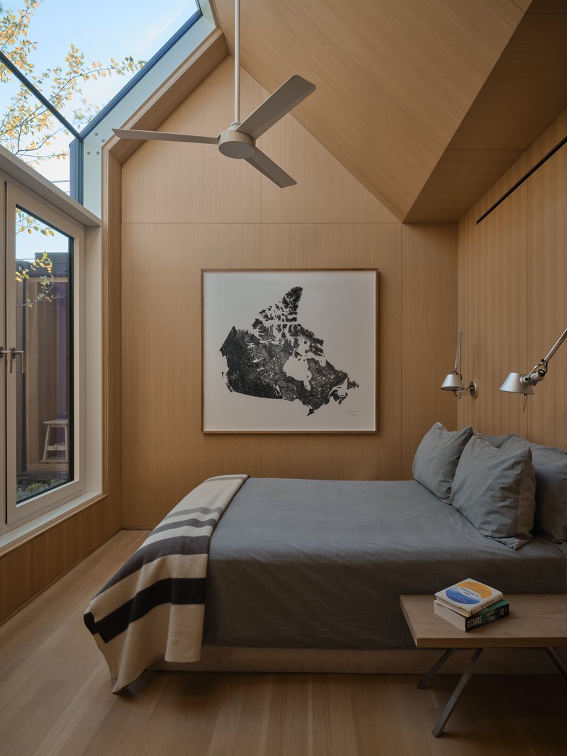Bedroom with light wood paneling and vaulted ceiling, skylight bringing in afternoon sun