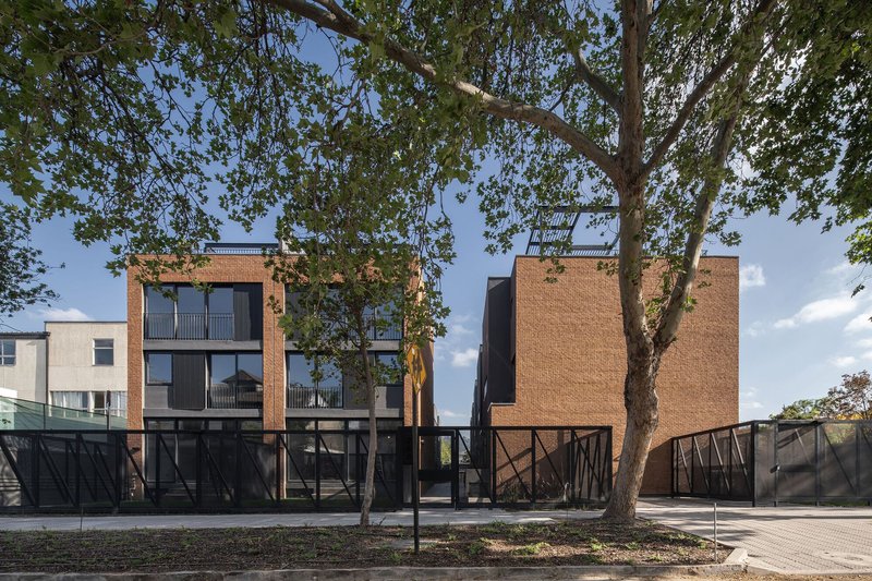 Street view of the brick facade with raised steel-braced ground floor beneath mature tree canopy