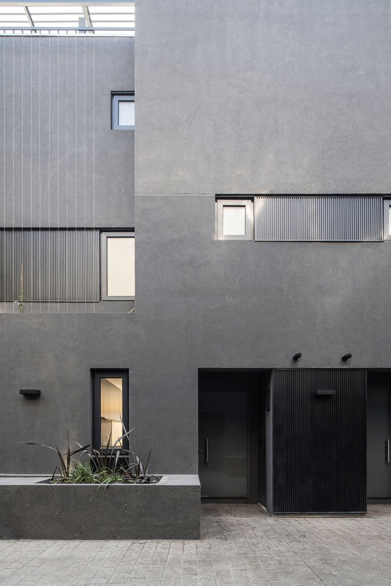 Courtyard facade composition with grey render, corrugated metal cladding panels and punched window openings