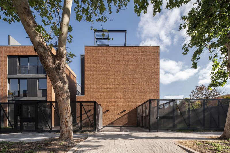 Brick volume with diagonal steel bracing and ramped entrance under afternoon clouds and tree branches