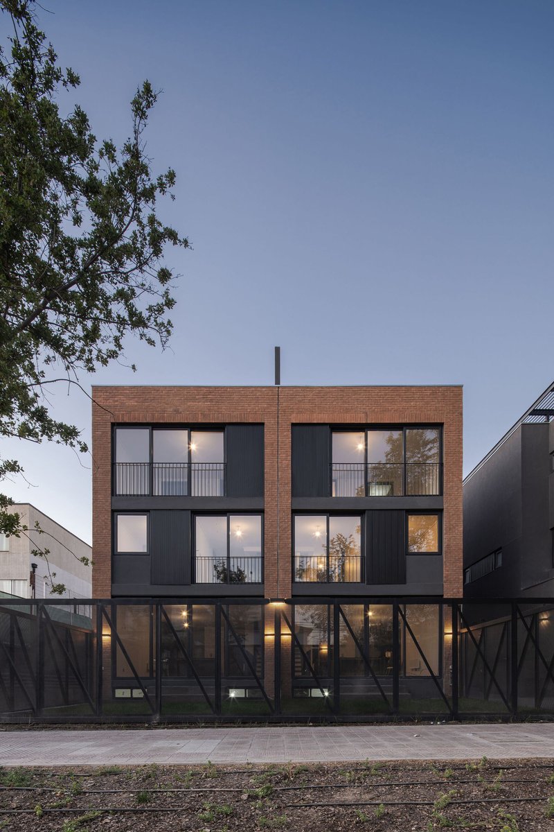 Street elevation showing the brick facade with recessed balconies and diagonal metal fence at dusk