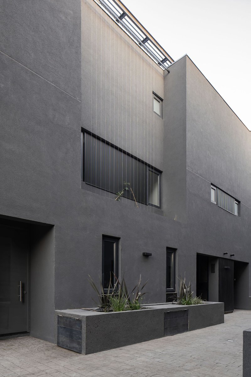 Courtyard facade showing stucco volumes with vertical metal screening and a raised concrete planter with dried grasses