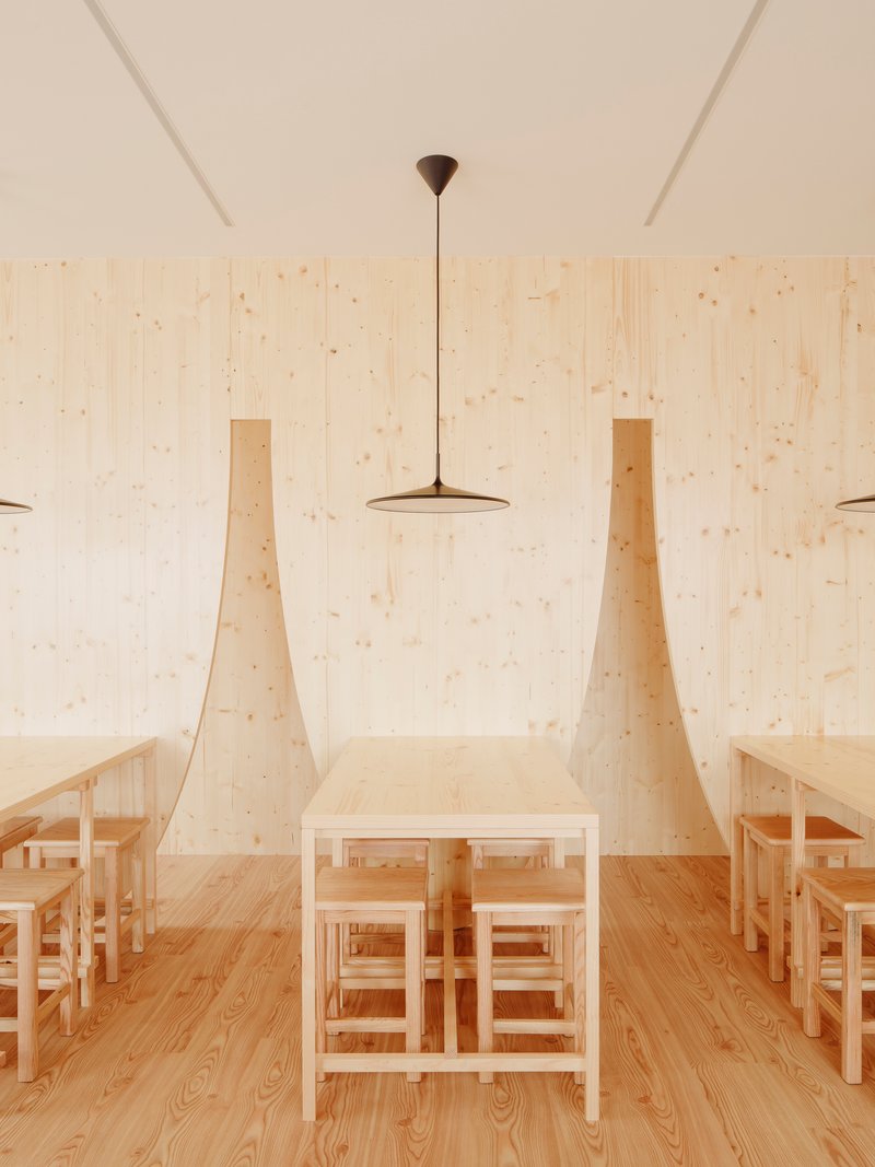 Central dining table flanked by tapered plywood wall fins under a flat disc pendant