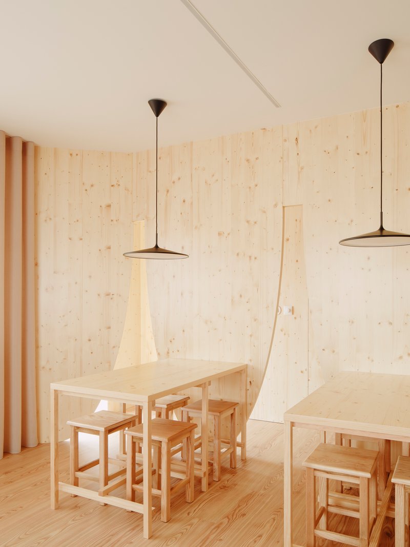 Dining tables with stools and pendant lights against pale plywood walls and vertical drapes