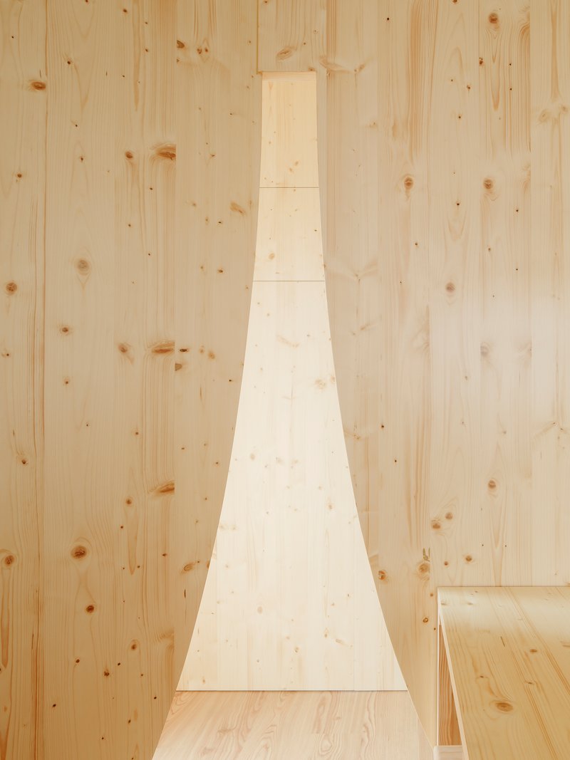 Narrow vertical window cut into pale timber wall beside plywood flooring