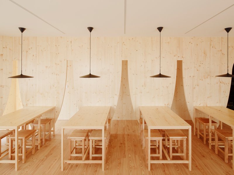 Angled timber partitions creating nooks for dining tables beneath flat pendant lights in a plywood-paneled room