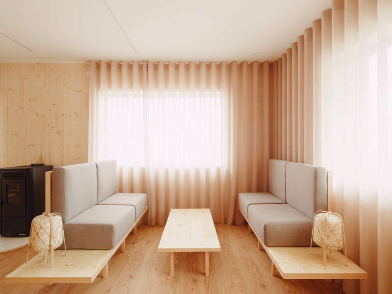 Corner seating area with upholstered benches and low table beneath pleated fabric curtains in warm light