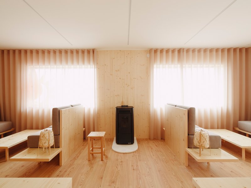 Central wood stove with white base flanked by windows with sheer curtains and timber privacy screens