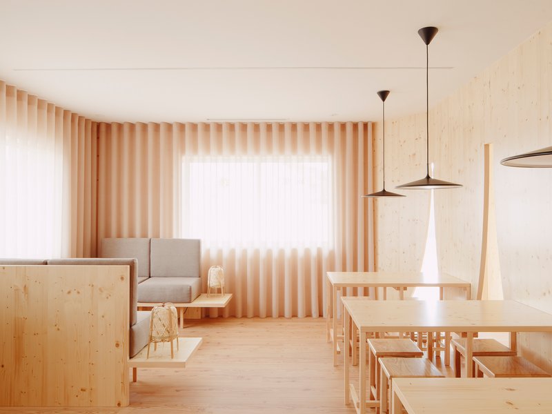 Light-filled dining area with pale timber furniture and vertical slatted curtains on corner windows