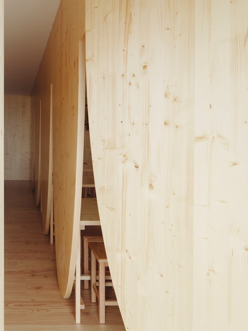 Glimpse through curved partition wall showing stacked stools and concrete in background