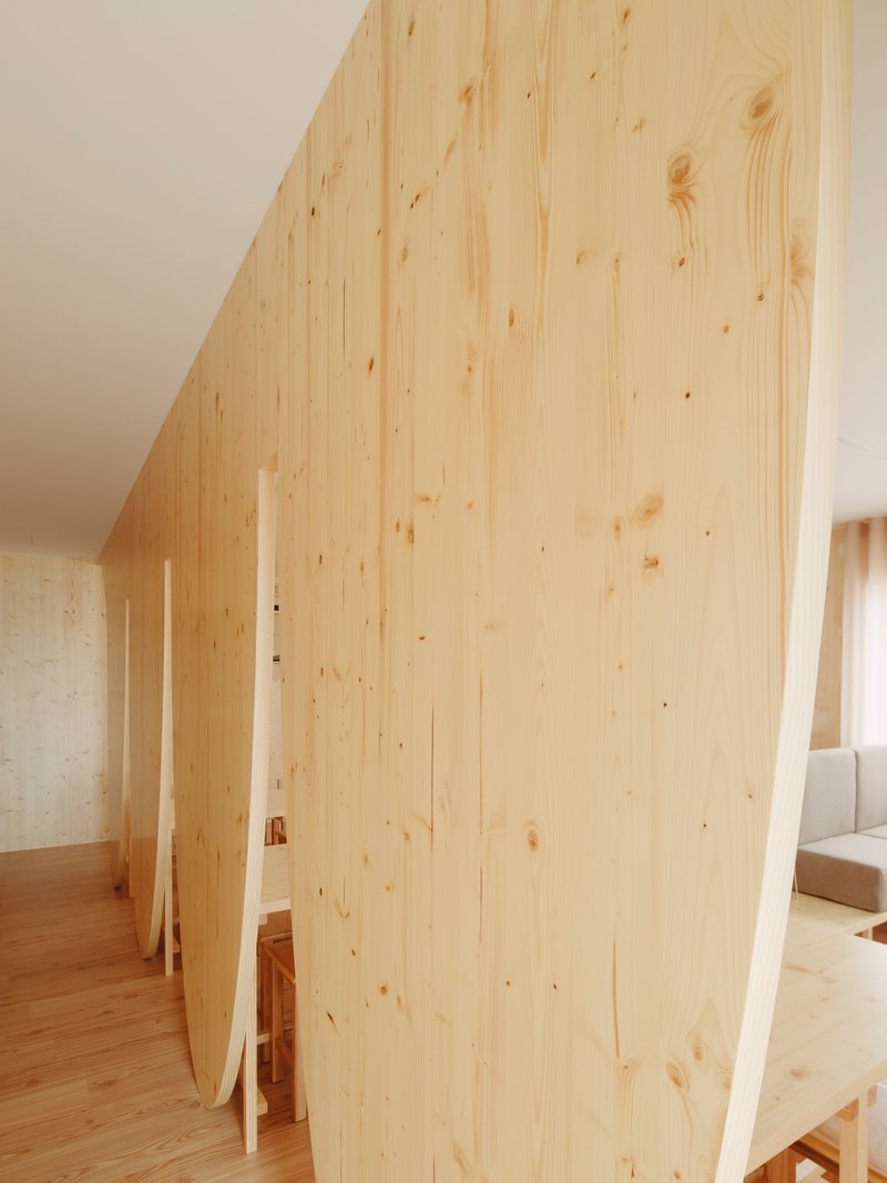 Light wood partition wall with vertical planks curving through an interior with timber flooring