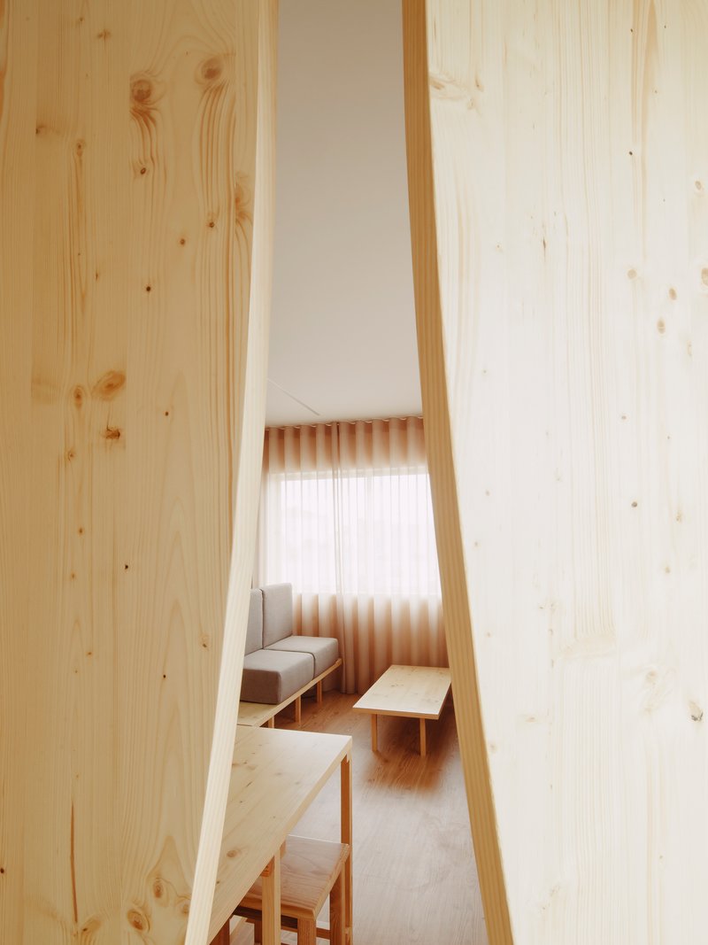 View through a narrow vertical opening in the wood partition toward a seating area with pleated curtain