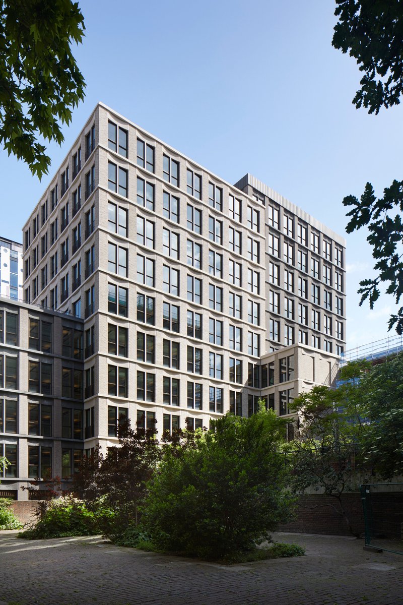 Multi-story facade with regular window grid and planted landscaping framed by tree canopy