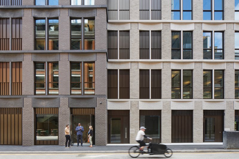 Street elevation showing mixed brick and stone facade with pedestrians and a cyclist passing by