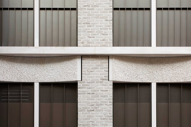 Facade detail showing white brick piers between grey metal panels and scalloped concrete spandrels