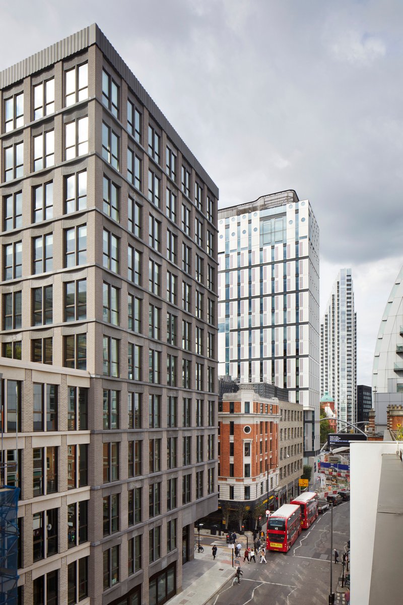Street view of two residential towers with pedestrians and red buses below cloudy skies