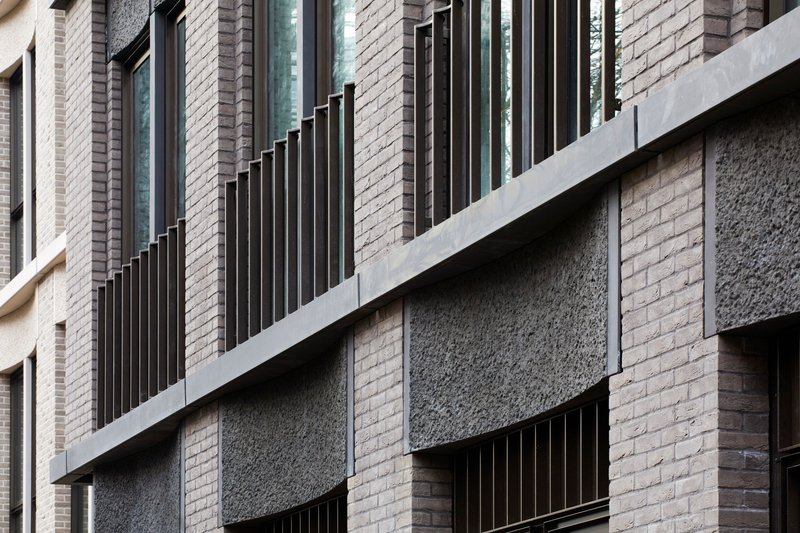 Facade composition mixing textured brick panels, black metal fins and smooth concrete slabs