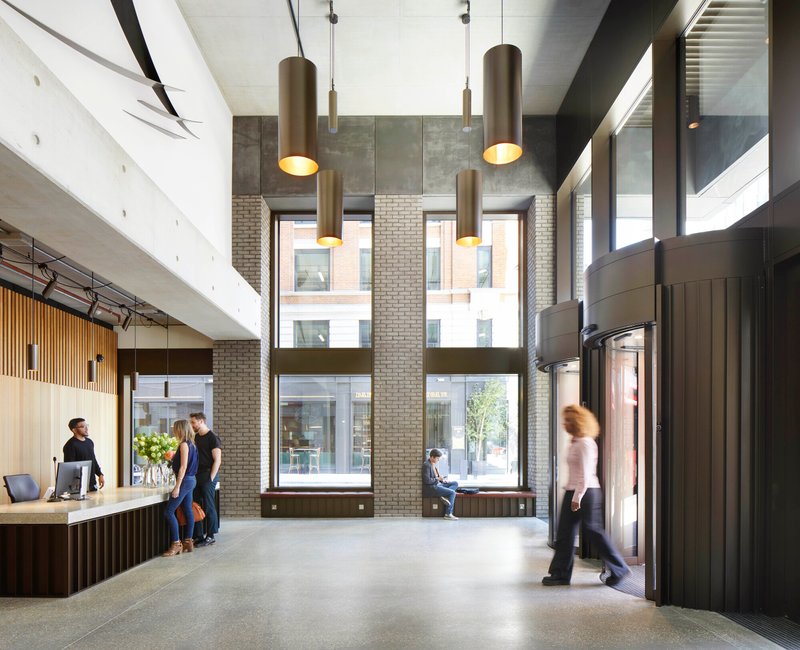 Double-height reception lobby with cylindrical bronze pendant lights and floor-to-ceiling windows overlooking the street