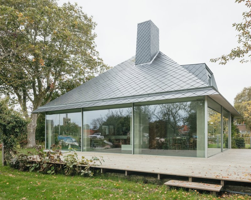 Glass-enclosed pavilion with sliding panels raised on a timber deck surrounded by lawn