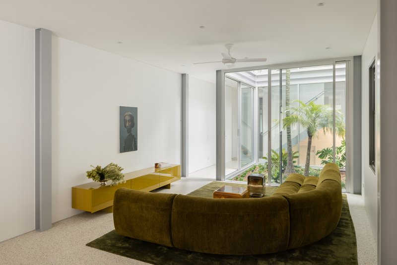 Living room with terrazzo floor opening onto a glazed courtyard planted with palms