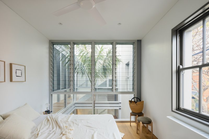 Bedroom with louvered windows opening to a courtyard planted with palms and grasses