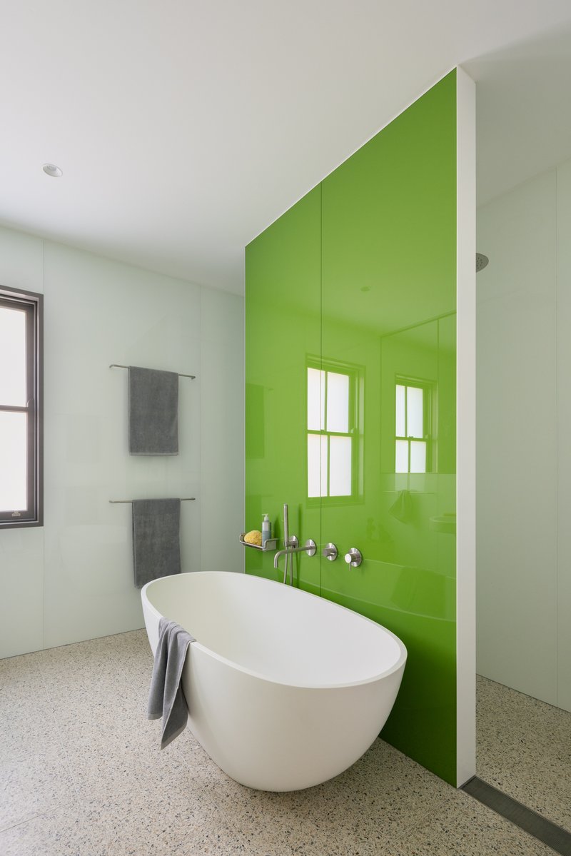 Freestanding bathtub positioned against a lime green glass wall with wall-mounted faucets